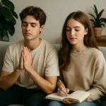 A 20-year-old boy sitting with hands together in a prayer pose and a girl writing in a journal, both calm and relaxed on a sofa surrounded by plants, symbolizing mental detox and mindfulness